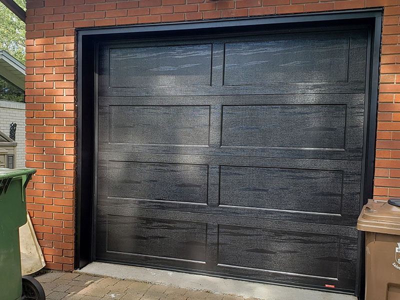Porte de garage Shaker-Plat XL Noir sur une maison en brique rouge.
