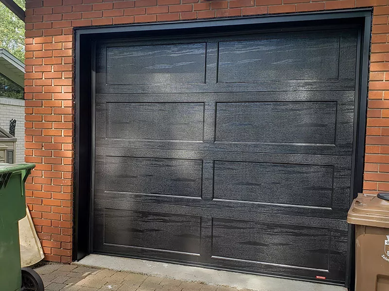 Porte de garage Shaker-Plat XL Noir sur une maison en brique rouge.